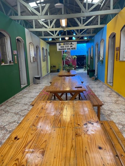 Espaço interno de um hostel, com mesas e cadeiras