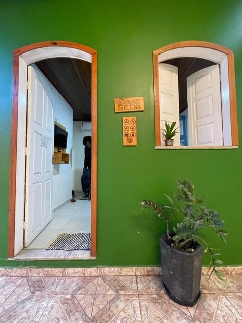 Entrada de uma casa com paredes verdes e portas e janelas brancas com detalhes laranjas