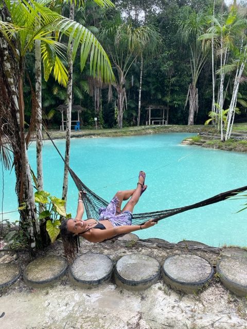 Mulher em uma rede de frente para uma lagoa de água azul cristalina