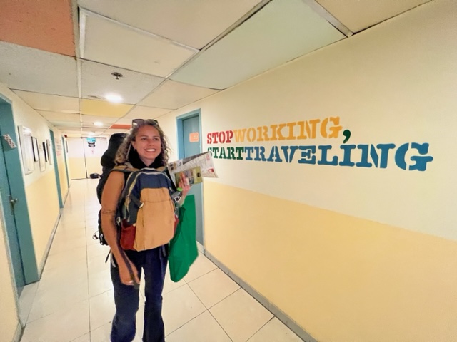 Mulher ao lado de parede com escrita "stop working, start travelling".